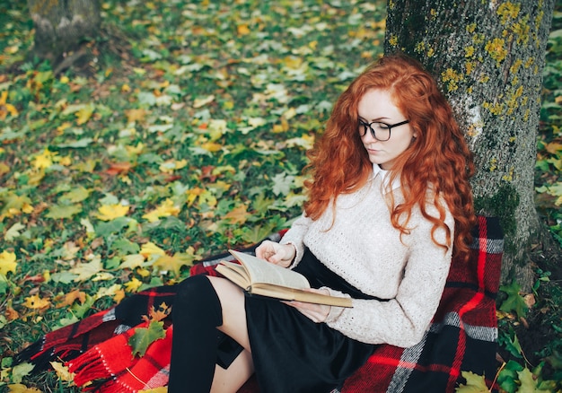 chica pelirroja leyendo el libro en el parque de otoño