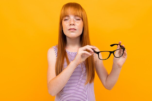 Chica pelirroja con mala vista sobre un fondo amarillo