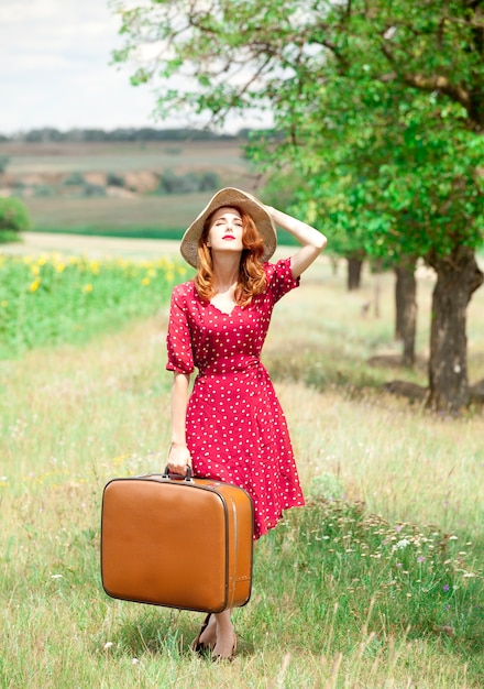 Chica pelirroja con maleta al aire libre.