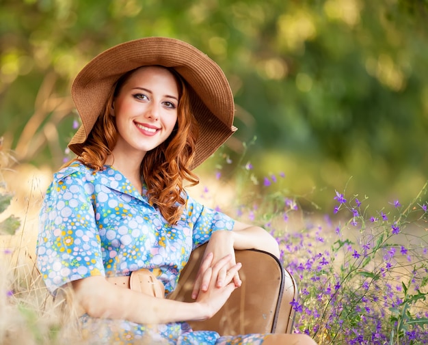 Chica pelirroja con maleta sentada en la hierba de otoño