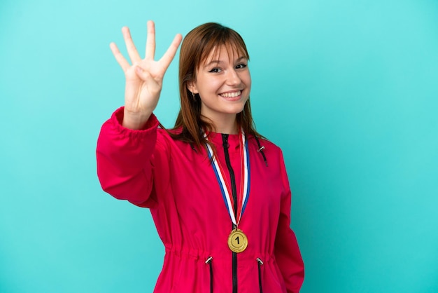 Chica pelirroja con medallas aisladas o fondo azul feliz y contando cuatro con los dedos