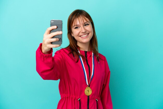 Chica pelirroja con medallas aislado o fondo azul haciendo un selfie