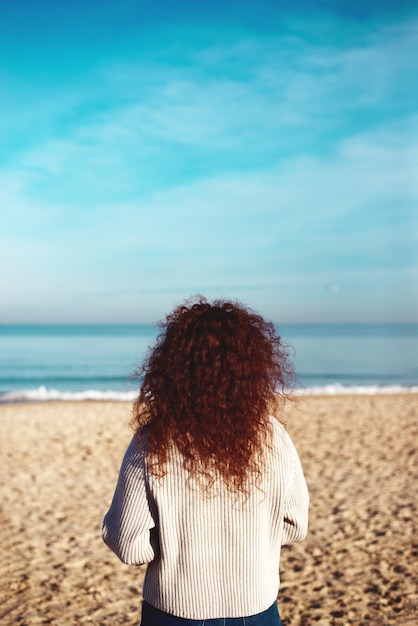 Una chica pelirroja mira al mar. Playa.