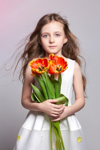 Chica pelirroja de moda con tulipanes en las manos. Foto de estudio sobre fondo de color claro. Cumpleaños, vacaciones, día de la madre, primer día de clases.