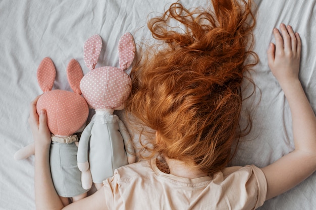 Chica pelirroja con muñecas en la cama.