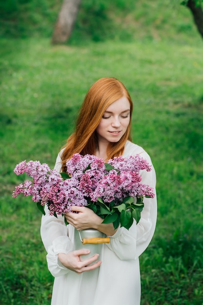 Chica pelirroja con un ramo de lilas en un jardín de primavera