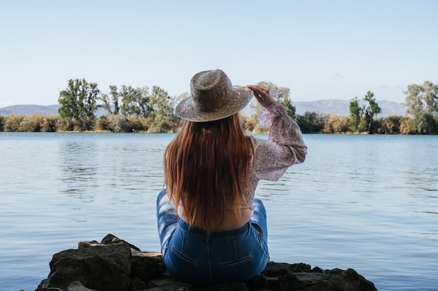 Chica pelirroja sentada en una piedra mirando un río