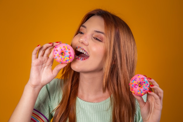 Chica pelirroja sobre fondo amarillo comiendo deliciosas donas de colores.