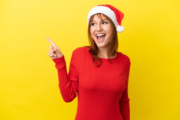 Chica pelirroja con sombrero de navidad aislado sobre fondo amarillo con la intención de darse cuenta de la solución mientras levanta un dedo