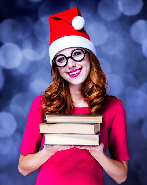 Chica pelirroja con sombrero de navidad con libros en gris