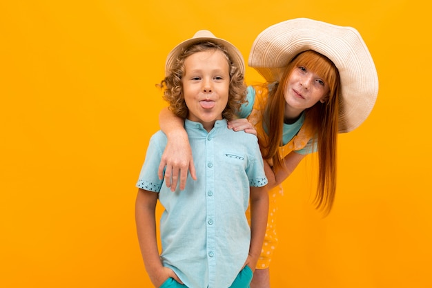 Foto chica pelirroja con sombrero de verano asoma por detrás de un niño