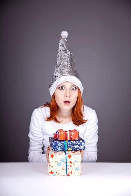 Chica pelirroja sorprendida en gorro de navidad con cajas de regalo.