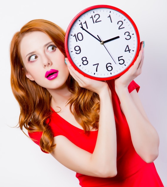 Chica pelirroja sorprendida en vestido rojo con gran reloj en blanco