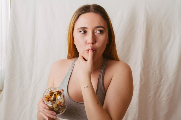 Chica pelirroja en sujetador deportivo lamiendo su dedo después de comer un bocadillo saludable de frutas secas