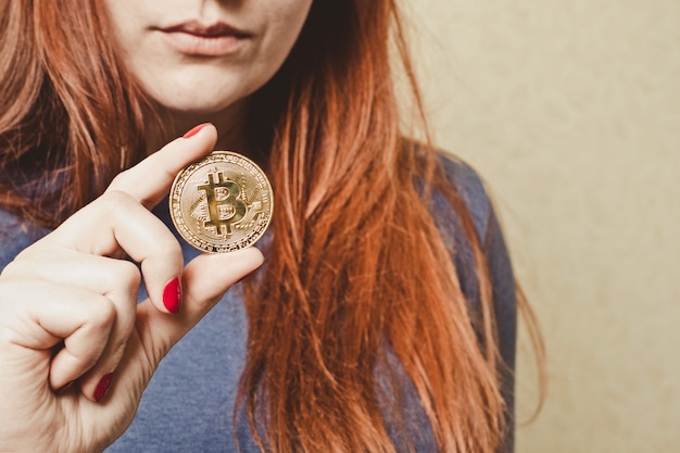 Chica pelirroja tiene moneda de oro bitcoin en su mano