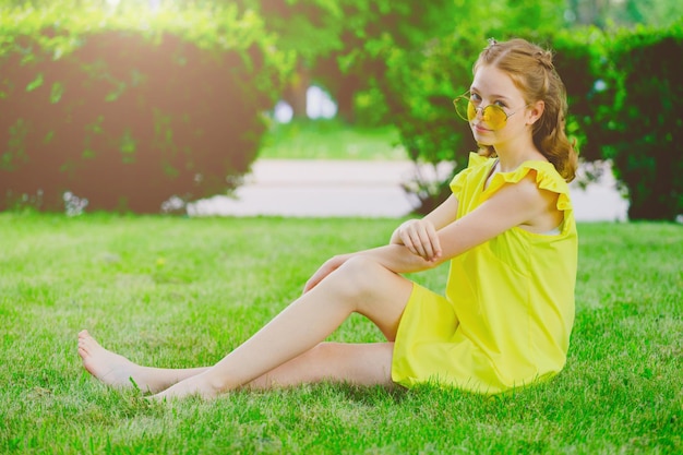 Chica pelirroja con un vestido amarillo en el césped del parque en verano Foto de alta calidad