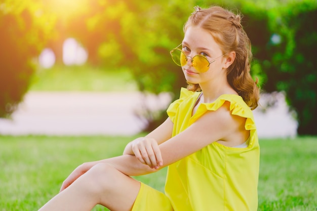 Chica pelirroja con un vestido amarillo en el césped del parque en verano. Foto de alta calidad