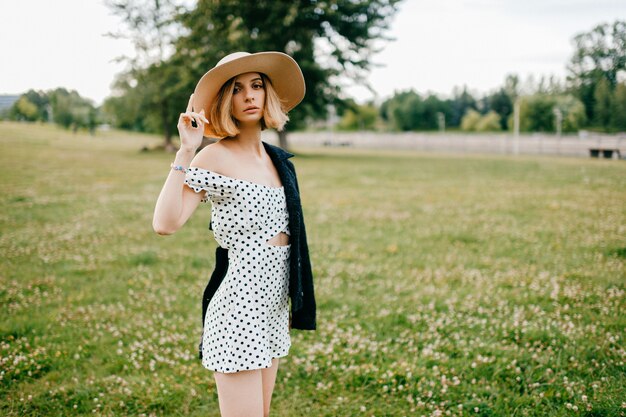 Chica de pelo corto rubio elegante elegante con sombrero posando en el campo