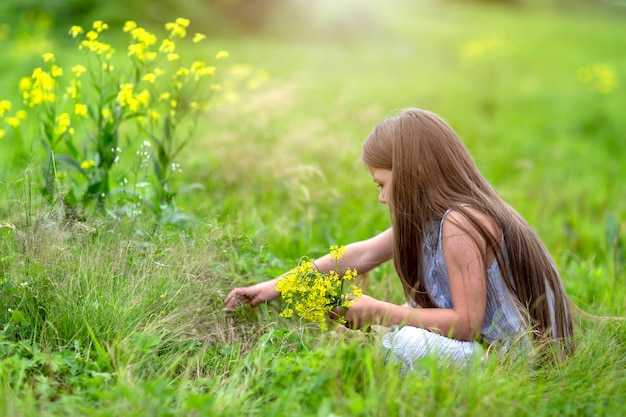 Una chica con el pelo largo en un campo olfateando flores amarillas Alta calidad