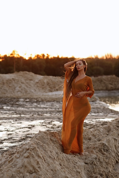 Chica con el pelo largo en una capa transparente en la arena en el verano al atardecer