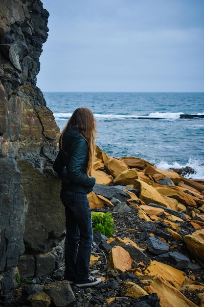 Chica con el pelo largo cerca de las rocas a la orilla del mar.