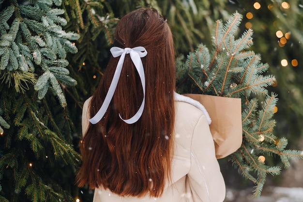 Una chica con el pelo largo se encuentra de espaldas en un bosque de invierno con un ramo de ramas de abeto Invierno nevado