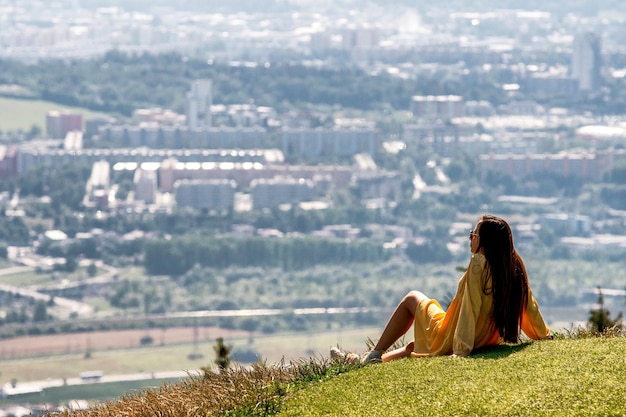 Chica de pelo largo sentada en la cima de la colina y mirando hacia la ciudad