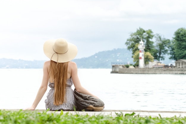 Chica con el pelo largo y un sombrero sentado en el muelle con una mochila