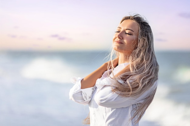 Una chica con el pelo largo en un traje de baño azulado y una camisa pasa por su cabello en la orilla del mar