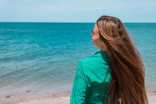 Una chica con el pelo largo con un vestido verde en la playa. vacaciones en la playa