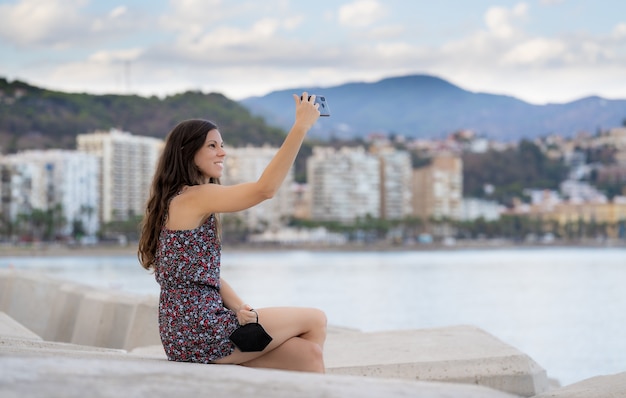 Chica de pelo muy largo con vestido tomar un selfie en el puerto con fondo de mar