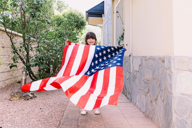 Chica de pelo negro sosteniendo y ondeando una bandera de los Estados Unidos en el jardín de su casa Concepto de celebración día de la independencia Estados Unidos de América 4 de julio patriotismo y orgullo estadounidense