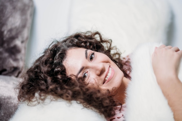 Chica de pelo rizado abrazando una almohada antes de acostarse Día Mundial del Sueño