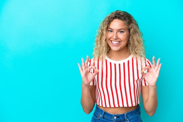 Chica con el pelo rizado aislado sobre fondo azul mostrando el signo de ok con las dos manos