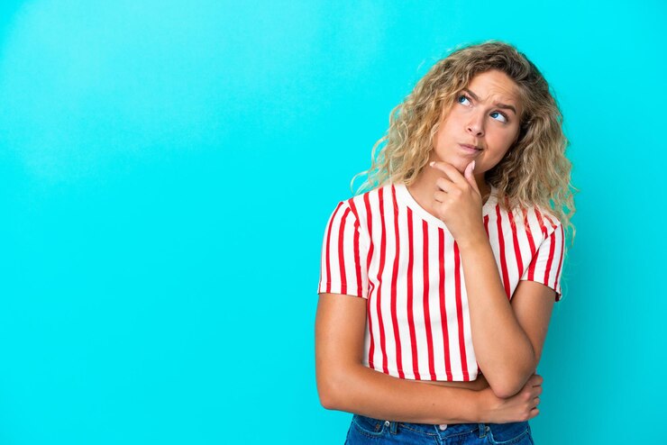 Foto chica con pelo rizado aislado sobre fondo azul teniendo dudas