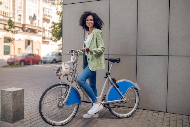 Chica de pelo rizado en ropa de moda con una bicicleta