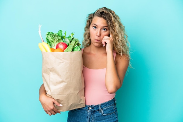 Chica con el pelo rizado sosteniendo una bolsa de compras aislada en un fondo verde pensando en una idea