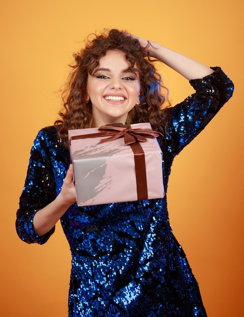 Chica de pelo rizado sosteniendo su caja de regalo y riendo Foto de alta calidad