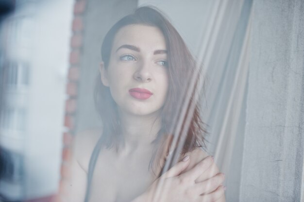 Chica de pelo rojo con un gran busto en sujetador negro en el espejo de la ventana.