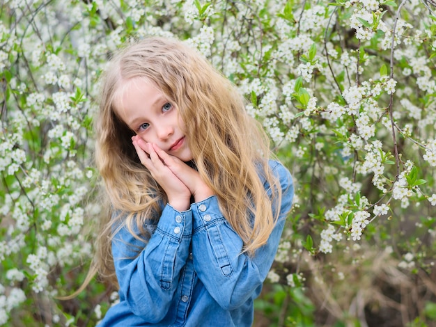 Chica con el pelo suelto en una camisa vaquera en un jardín de cerezos en flor