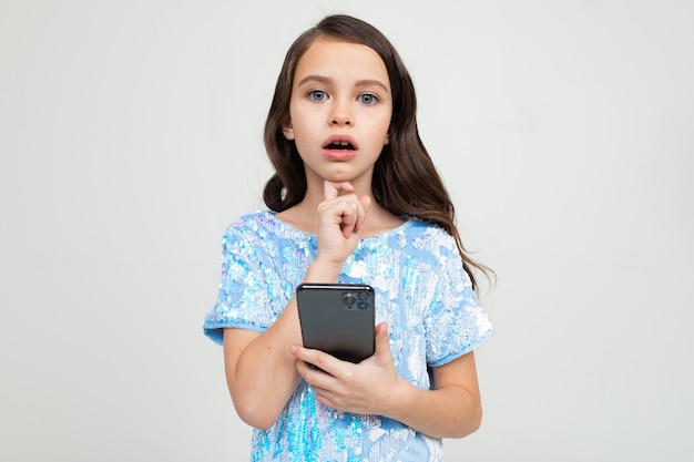 Chica pensativa con la boca abierta sostiene el teléfono en un estudio blanco