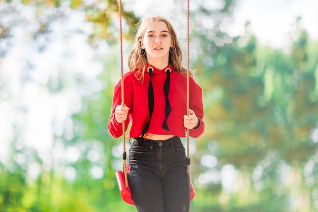 Chica pensativa en un columpio en el bosque de verano