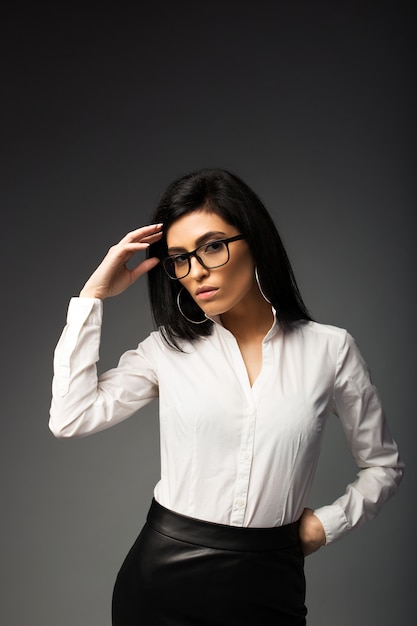 Chica pensativa morena con gafas, en una blusa blanca con una falda de cuero negro.