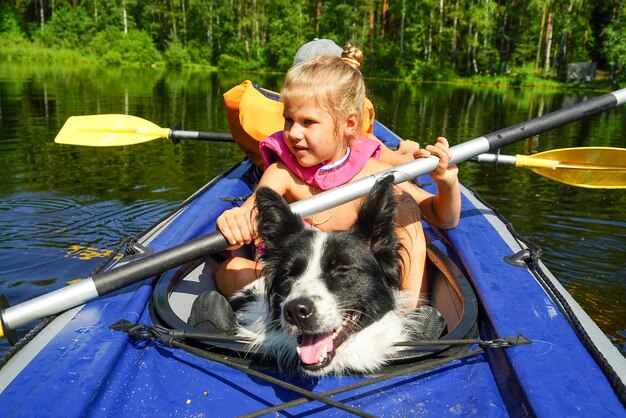 Chica con un perro sentado en un kayak en el lago.