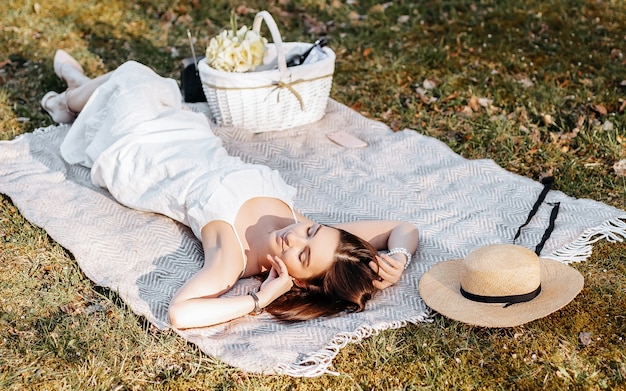 Chica de picnic con un sombrero de paja en la primavera en el parque. Morena con cabello largo yace sobre un plaid sobre un fondo de naturaleza veraniega.