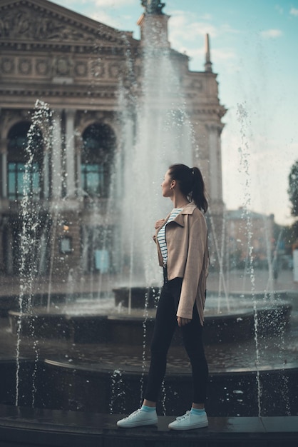 Chica de pie cerca de la fuente Fin de semana en Europa Marco vertical