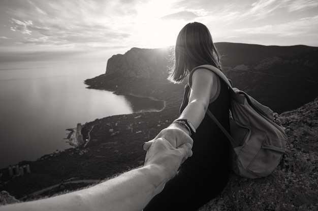 Chica de pie en la cima de la montaña con vistas al mar azul. Sígueme - POV. Pareja disfrutando de una caminata en la naturaleza. El concepto del viaje al encuentro de nuevos descubrimientos.