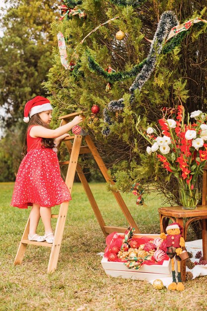 Chica de pie en una escalera decora el árbol de Navidad