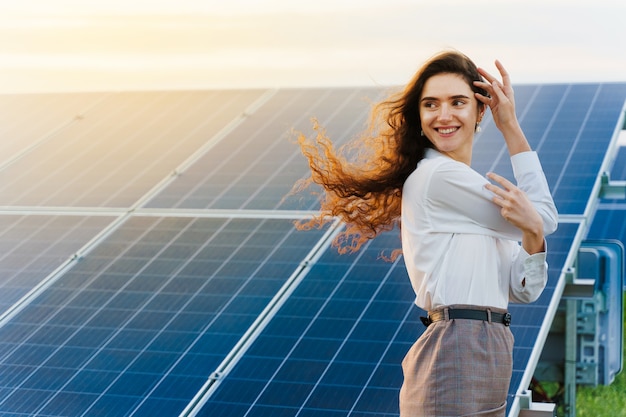 Chica de pie junto a las filas de paneles solares durante la puesta de sol