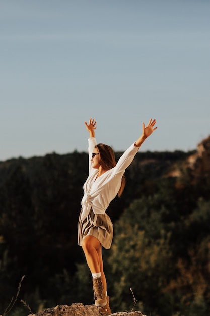 Chica de pie sola en piedra grande en un día soleado en las montañas